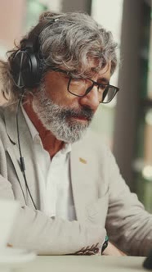 Mature businessman and headphones, sits in an outdoor cafe and works using tablet