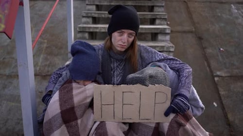 Homeless Mother with Two Children is Sitting on the Stairs in Abandoned Place and Holding Sign Help
