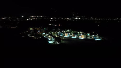 Drone orbiting vacation homes with illuminated pools, night in Rhodes, Greece