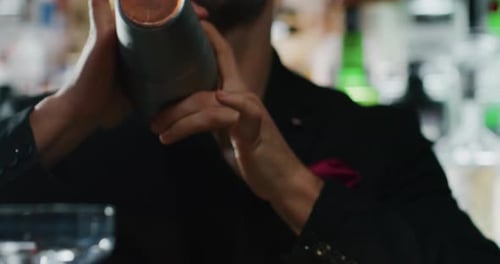 Close up of a professional bartender is preparing an alcoholic cocktail with ice cubes in a shaker