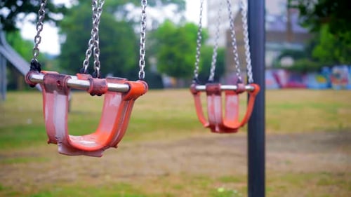 Baby chair swing moving slowly in an empty park playground, lockdown emptiness scene