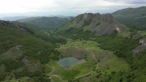 Flying over beautiful green mountains. In the background, stone cliffs with snow are visible.