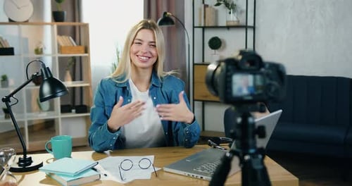 Woman blogger sitting in front of camera while recording video for her internet channel and gesturin