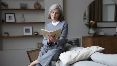 Senior Woman Reading Book on Couch at Home