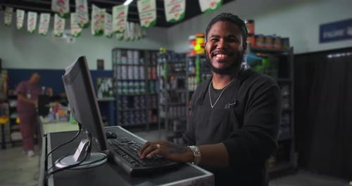 One Smiling Black store clerk interacting with customers, computer on desk