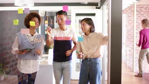 Três colegas criativos diversos, homens e mulheres, discutindo ideias em uma parede de vidro, em câmera lenta