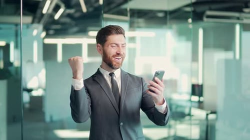 Excited Businessman Celebrates Success With Phone in Office