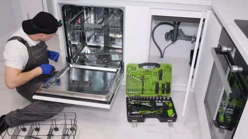 Ein junger Mechaniker repariert einen kaputten Geschirrspüler in einer modernen Küche