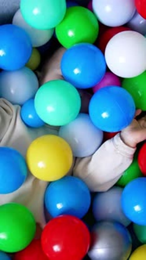 Baby boy lies hiding in the colorful balls in a dry pool.