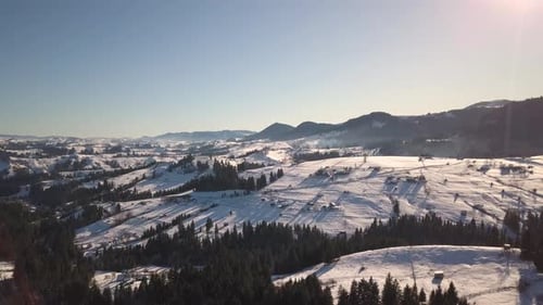 Luftaufnahme eines kleinen Dorfes mit verstreuten Häusern auf schneebedeckten Hügeln im Winter und in nackter Dunkelheit