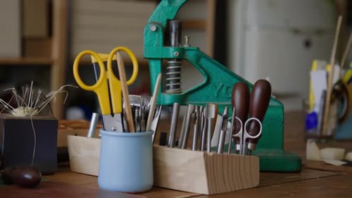 Containers and Wooden Holds for Leather Crafting Tools on Table in Workshop