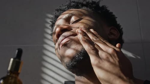Close-up of Black Young Man Applying Facial Serum Directly with Dropper