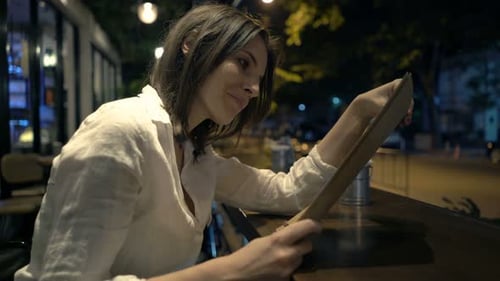 Woman Reading Menu Sitting In Cafe At Night