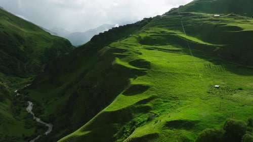 Lush Green Slopes of a Mountain with a Small Settlement Under a Cloudy Sky in a Tranquil Environment