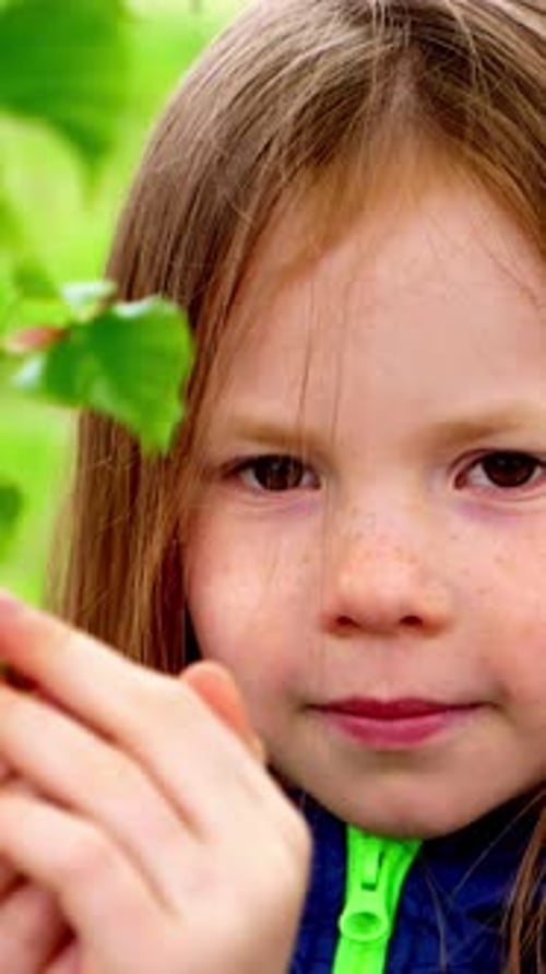 Young Girl with Long Hair Holding a Green Leaf Showcasing Curiosity and Connection to Nature