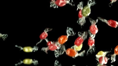 Colorful wrapped candies falling on reflective black surface