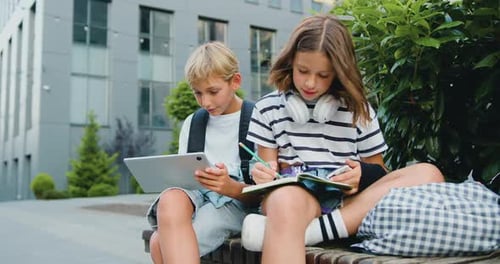 School students friends outdoors using digital tablet computer . Kids sitting on bench and play