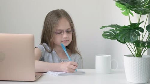 School Girl Wearing Glasses Sitting at Table Doing Homework