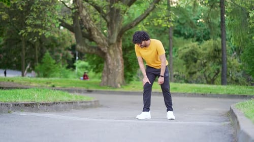 Young adult runner athlete with muscle pain in an city park. Man massaging stretching, trauma injury