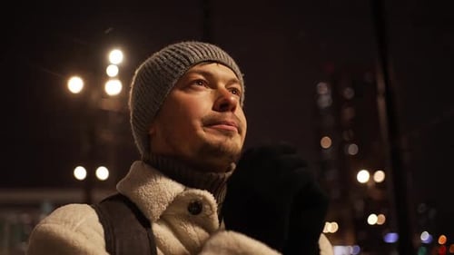 Man Warms Hands on Snowy Urban Night