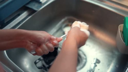 Hand washing utensil at the sink in the kitchen. People cleaning chores at home