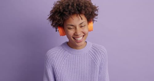 Lächelnde, frohe, dunkelhäutige junge Frau mit lockigem Haar fühlt sich sehr glücklich