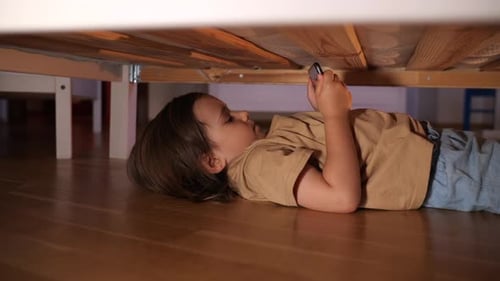 Child Lying Under Bed Looking at Smartphone