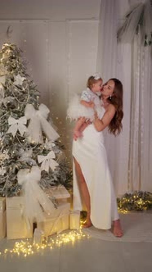 Mother Holds Baby Dressed in Festive Clothes Next to Decorated Christmas Tree Family New Year
