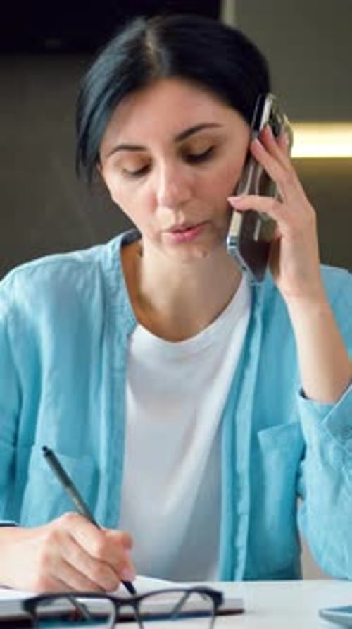 Woman Talking on Phone While Writing Notes
