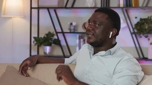 Man Talking with Wireless Earbuds on Sofa