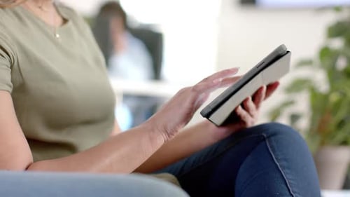 Midsection of caucasian casual businesswoman using tablet in office, slow motion