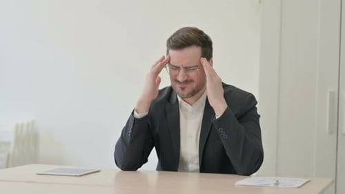 Man in Suit Massaging Temples at Desk
