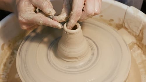 Hands shaping clay on a spinning pottery wheel