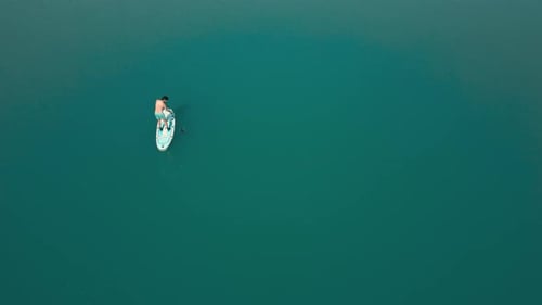 Aerial drone flying over a man doing stand up paddle in a blue water lake with mountains