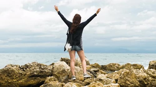 Wonderful Woman Stands On Rocks Raises Her Hands And Looks Out To Sea
