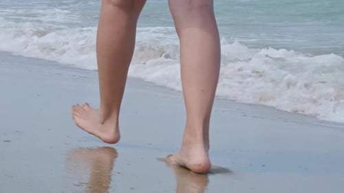 Woman's Feet Walking On Sandy Beach Barefoot Washed By Ocean Waves In Summer. - close up, crop