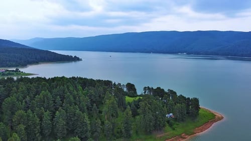 Lake with Clear Water and Stone Shore in Spruce Forest with Fir Trees Against a Daytime Sky