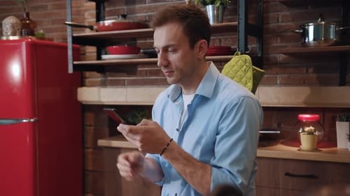 Young Adult Man Using Mobile Phone in Kitchen