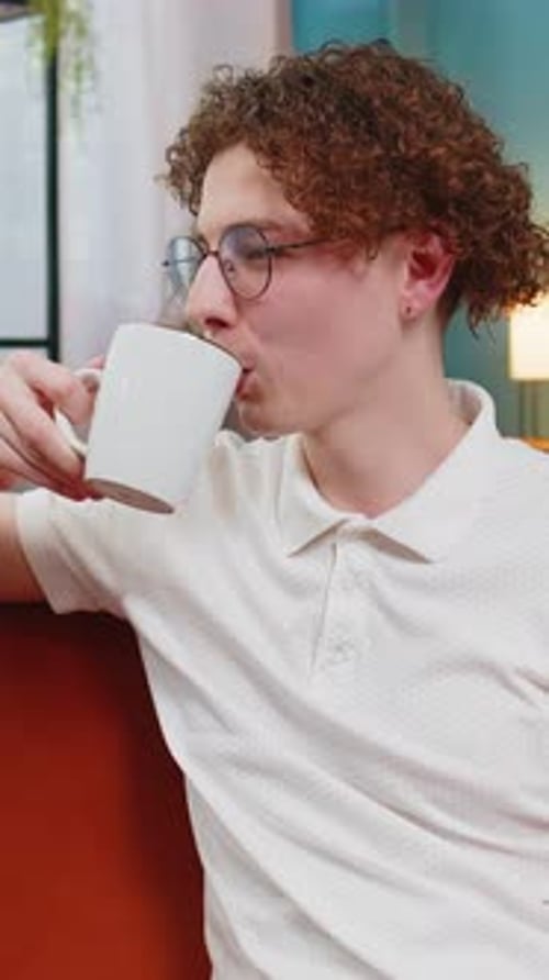 Young Man with Curly Hair Drinks from Mug
