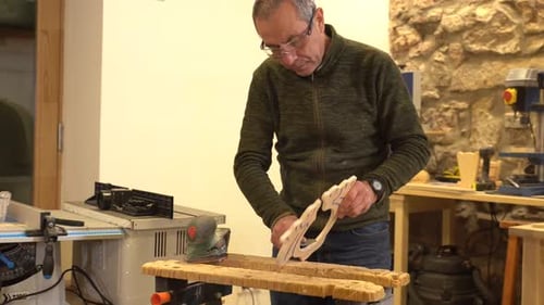Mature artisan polishing a piece of wood using an electric tool in a workshop