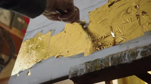 Ein älterer Künstler im Rollstuhl trägt Gold auf das Ölgemälde auf