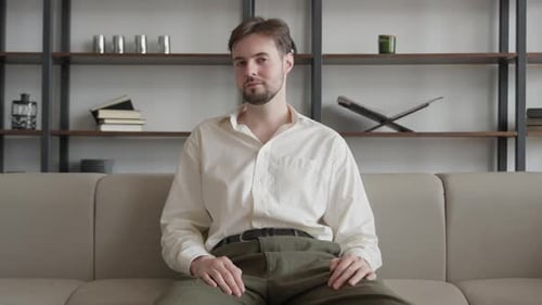 Successful Young Guy Sitting onCouch in the Office and Smiling at the Camera