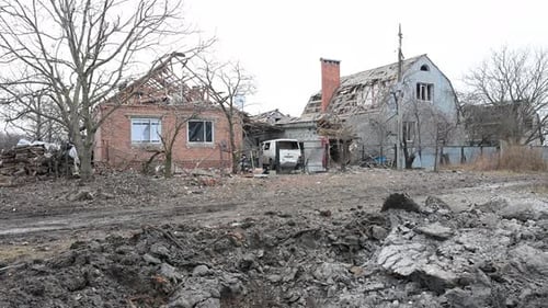 Tilt-down to a missile crater on a muddy street, revealing a Ukrainian village destroyed by a blast.