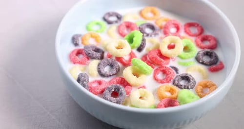 Breakfast cereal falling into bowl with milk on light table, closeup