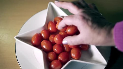 Tomatoes in shaped star dish with old woman hand taking one delicately.