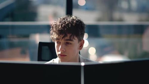 Young man is working in a computer in an office, windows on the background