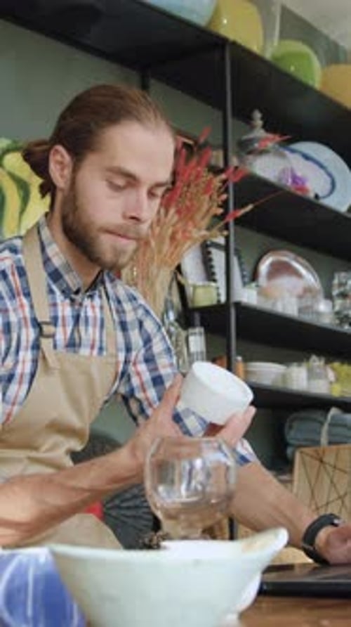 Goodlooking Purposeful 30Aged Bearded Seller Sitting at the Laptop in Cozy Gift Shop and Checking