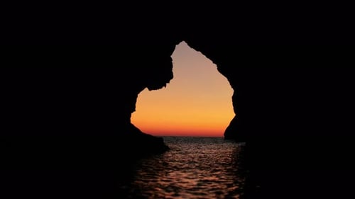 Malerischer Blick auf den Sonnenuntergang im Sommer über dem Meer durch ein Loch in der Höhle