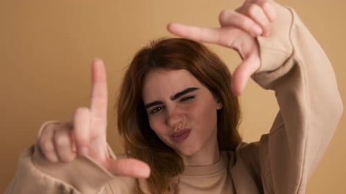 Cheerful Woman Showing Frame Gesture with Fingers in Studio