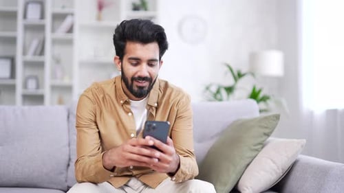 Smiling Man Using Smartphone on Sofa Indoors